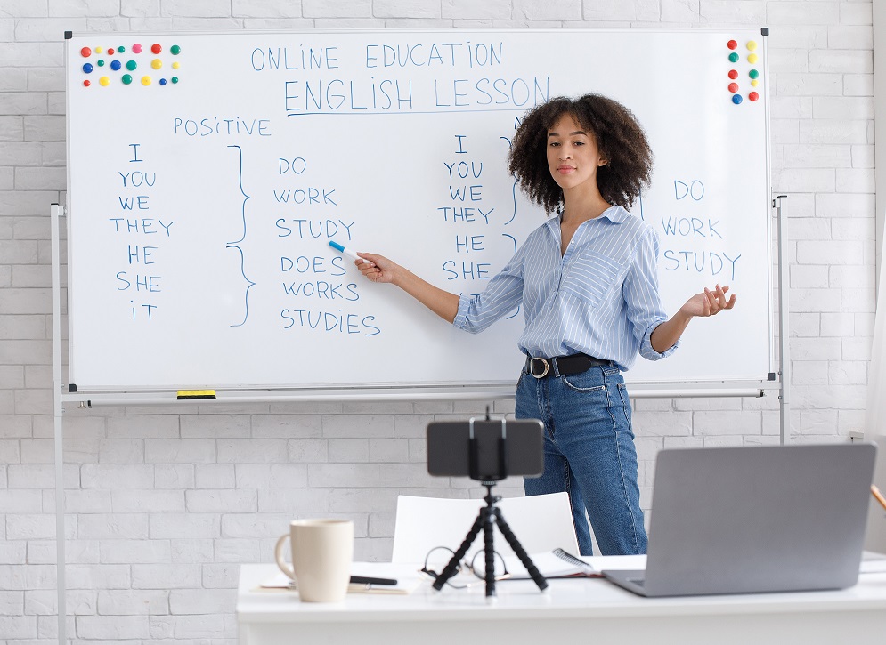 English teacher. Portrait of african american woman, writing on board in classroom and makes video for students on webcam in interior of living room